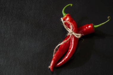 Siyah zemin üzerinde iki kapsül olgun kırmızı biber. Sebze bahçesinden taze koparılmış ve sicimle bağlanmış. Yeni acı biber mahsulü.