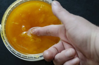 Adam işaret parmağını silindirik plastik bir kapta organik sarı arı bala daldırıyor. Doğal arı balı, arıcılık.