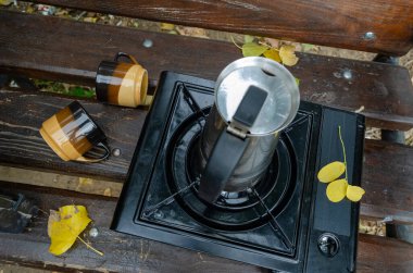 Geyser metal kahve makinesi ve park bankında taşınabilir gaz sobası. Piknik veya gezi sırasında doğal kahve yapma süreci. Yaşam biçimi.