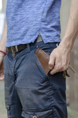 Genç adam cebinden cüzdanı çıkardı. Eli mavi pantolonunun cebinden kahverengi deri bir çanta çıkardı..