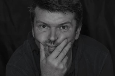 Vücut dili kavramı. Kafasını yumrukla destekleyen yetişkin bir adamın siyah beyaz portresi. Sıkılmış orta yaşlı bir adam..