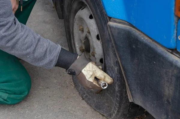 Tire service, car service concept. Car mechanic manually unscrews the bolts on the wheel. Replacing a flat tire. Side view. Selective focus.