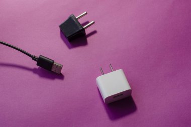 Siyah ve beyaz değiştirilebilir DC ve AC prizleri. ABD ve Avrupa için duvar adaptörleri ve pembe arka planda USB veri kablosu.