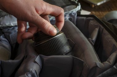 Adamın eli kamera lensini kamera çantasının içine yerleştiriyor. Fotoğraf ekipmanları için gri özel sırt çantası. Seçici odak.