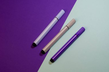 İki tonluk arka planda pastel renkli keçeli kalemler. Çizim için üç işaret. Yakın çekim, seçici odaklanma.