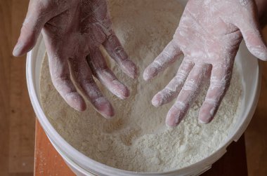 Erkek elleri beyaz unla fırçalanmış, plastik kovada buğday unu var. Ev yapımı yemek pişirmek. Yukarıdan bir açıdan bak. Seçici odak.