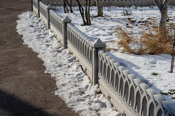 Gray Decorative fence near the snow-covered lawn. Beautiful Low concrete barrier. Sunny winter day. No people.