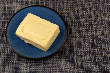 Dörtgen halinde işlenmiş peynir dilimi ve kot pantolon arka planında mavi bir fincan tabağı. Süt ürünleri, yiyecek. Boşluğu Kopyala