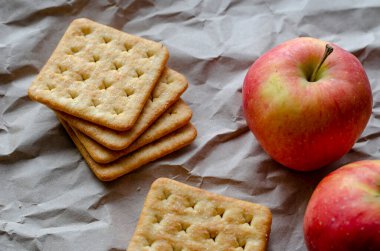 Olgun kırmızı elmalar ve buruşuk ambalaj kağıdının üzerinde duran kare krakerler. Okul yemeği konsepti. Bir açıdan yan bakış. Seçici odak.