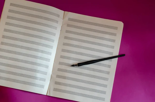 Black fountain pen and open music notebook on purple background. Musical creativity. Flat lay. Copy space.