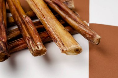 Useful dried chewy treats for pets in close-up. Dried bovine penis, bully sticks, beef pizzle for dogs on brown and white background. Focus on the foreground.
