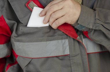 Göğüs cebinden beyaz bir akıllı telefonu çıkaran bir adamın yakın plan fotoğrafı. İş için özel kıyafetler giyen bir adam. Kırmızılı özel gri üniforma. Ön manzara. Seçici odak.