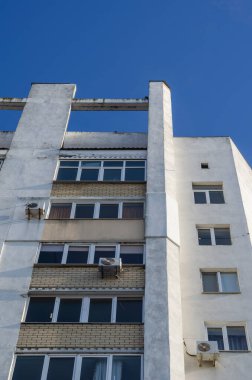 Mavi gökyüzüne karşı apartmanın zemin manzarası. Güneşli bir günde balkonları ve kliması olan beyaz bir bina. Emlak, kiralama..