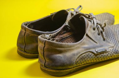 Sarı arka planda yırtık sarı yaz ayakkabıları. Bir çift ağır giysili deri ayakkabı..