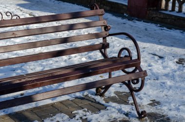 Winter City caddesinde boş, kahverengi bir bank. Tahta ve işlenmiş demir tezgah. Güneşli bir gün. Kimse yok..