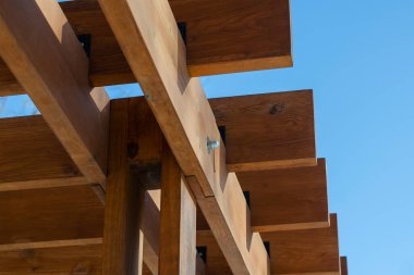 Mavi gökyüzüne karşı kahverengi ahşap kalasların soyut geometrik bileşimi. Açık hava çardağının bir parçası. Seçici odak.