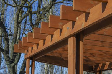 Mavi gökyüzüne karşı kahverengi ahşap kalasların soyut geometrik bileşimi. Şehir parkında bir çardak parçası. Seçici odak.