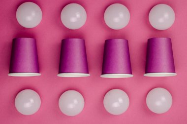 Kağıt bardaklar ve mercan zemininde beyaz küreler ile yaratıcı geometrik bileşim. Sekiz küre ve dört bardak. Düz Yat.