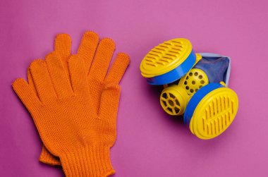 Sarı ve mavi solunum cihazı ve pembe arka planda koruyucu eldivenler. Gazlara (toz, duman, sis) veya zararlı gazlara karşı özel bir kişisel solunum koruma aracıdır. Seçici odak.