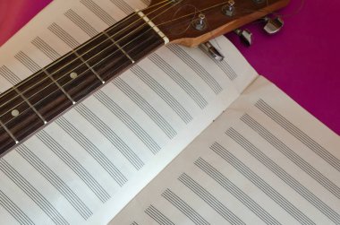 Akustik gitar klavye kafası ve mor arka planda açık bir defter. Müzikal yaratıcılık. Seçici odak
