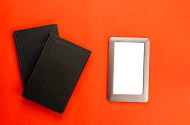 Kapalı ciltli kitaplar ve kırmızı arkaplan üzerine e-kitap. Bir kağıt kitap ve elektronik bir cihaz. Teknolojinin dayanıklılığı. Düz yatıyordu
