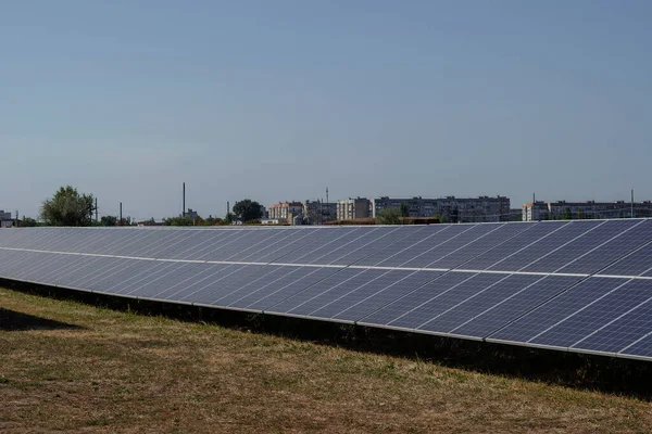 Solar electricity generation concept. Solar panels in a field on the outskirts of town. A residential area of the city in the background. No people. A sunny summer day