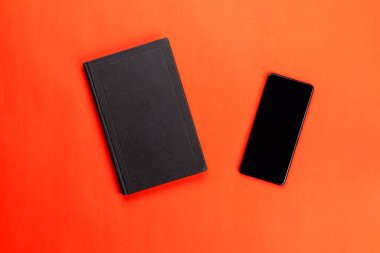 Siyah akıllı telefon ve kırmızı arka planda kapalı kağıt kitap. Kitap okumanın faydaları. Düz yatıyordu