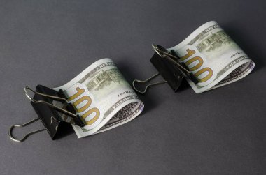 Gri arkaplandaki metal klasörüne 100 dolarlık banknot sıkıştırılmış yaratıcı soyut bir arka plan. Banknotlar yatay olarak ikiye katlandı. Yakın çekim, seçici odaklanma.