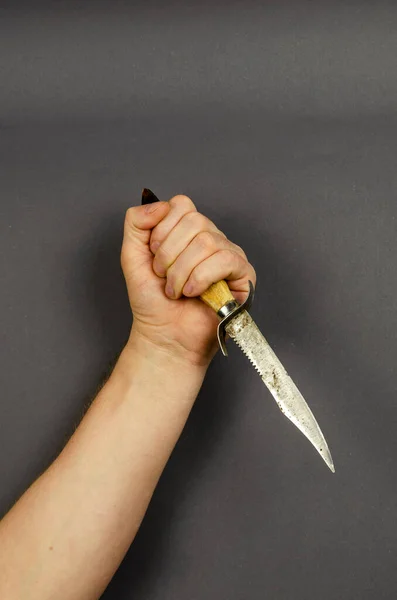 The hand is swinging to strike with a hunting knife on a gray background. Old Goat\'s leg knife with a guard. Stabbing from top to bottom. Side view.