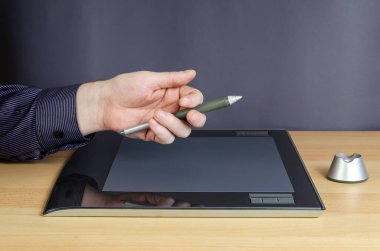 Grafik tabletinin üstünde özel bir kalemle bir adamın eli. Masada yatan tasarımcılar için profesyonel bir cihaz. Bir açıdan yan görünüm.