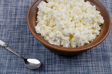 Kil bir kasede taze süzme peynir yakın plan. Bir kase kaymak ve mavi ve beyaz arka planda bir kaşık. Yemek hazır. Sağlıklı yiyecekler. Seçici odak.