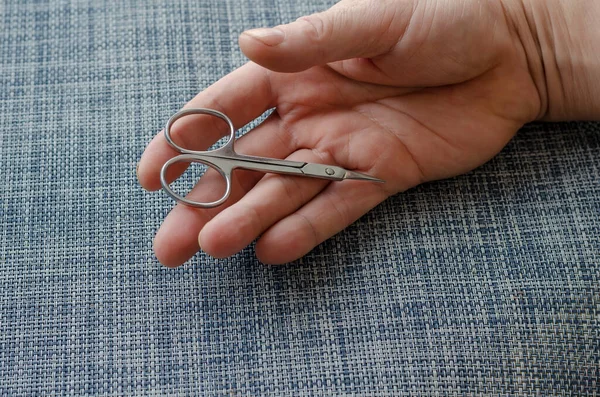 Manicure scissors lie in the open palm of an adult male. The hand rests on a blue surface. Close-up. Selective focus.