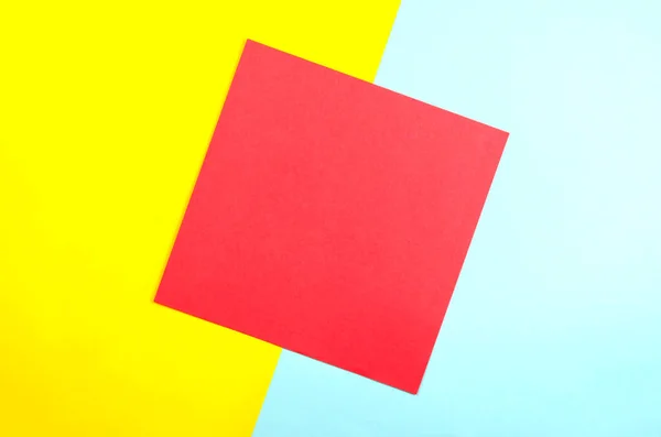 The red square on a pale yellow and blue background. Abstract geometric background of yellow, red and blue, created with overlapping paper. Top view, Flat Lay.