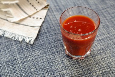 Bir bardak domates suyu ve mavi bir masanın üzerinde hafif püsküllü bir peçete. İçmeye hazır içecekler. Bir açıdan üstten bak. Seçici odak.
