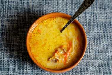 Karışık ekşi kremalı lahana çorbası ve kahverengi bir toprak kabında metal kaşık. Mavi ve gri bir masa örtüsü üzerinde hazır yemek çorbası. Yakın çekim, seçici odaklanma.