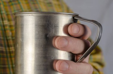 Sarı kareli gömlekli yetişkin bir adamın elinde metal bir kupa var. Orta yaşlı bir adam, Kafkasyalı, içeride. Yakın çekim, seçici odaklanma.