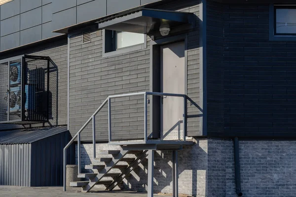 Modern industrial architecture concept. Facade of the Black industrial building. Door with staircase. Ventilation and air conditioning system on the wall. No people.