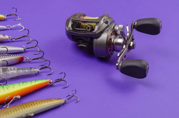 Artificial lures for fishing for predatory fish and a fishing reel on a blue background. Random wobblers are lined up. Baitcasting reel. Fishing, tackle. Selective Focus.