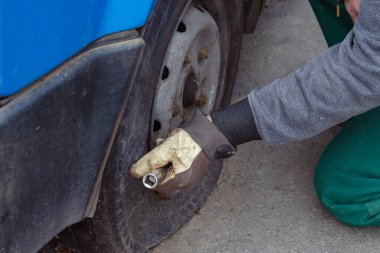 Lastik servisi, araba servisi konsepti. Araba tamircisi direksiyondaki vidaları elle söker. Patlak bir lastiği değiştirmek. Yan görüş. Seçici odak.