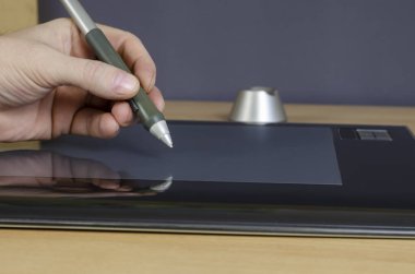 Grafik tabletinin ekranında özel bir kalemle bir tasarımcının el çizimi. Bir erkek eli ve yakın plan tasarımcılar için profesyonel bir cihaz. Bir açıdan yan bakış. Seçici odak.