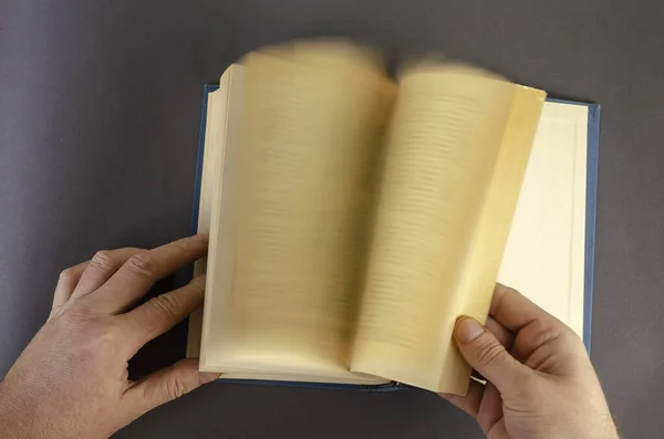 Blurred Motion Of Hand Turning Page Over gray Background. Male hands quickly leaf through an old book with yellowed pages. Middle-aged man, Caucasian.