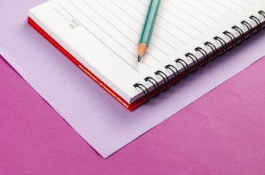 Pembe arka planda yaylı defter ve kalem aç. Beyaz not defteri ve yeşil kalem. Yakın plan. Seçici odak.