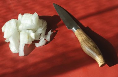 Ahşap saplı mutfak bıçağı ve kırmızı üzerine doğranmış çiğ soğan. Güneş ışığında küçük metal keskin bıçak. Bir porsiyon doğranmış soğan. Bir açıyla üstteki görünüm.