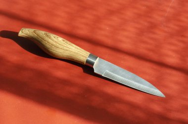 Mutfak bıçağı ve ahşap saplı kırmızı. Güneş ışığında küçük metal keskin bıçak. Bir açıyla üstteki görünüm.