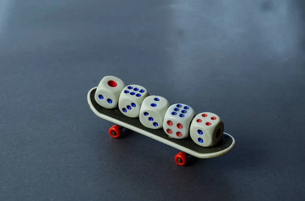 Old dice and finger skate on a gray background. Five random white dice on top of the mini skateboard. Side view. Selective focus.