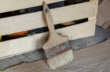 Eski bir fırça ahşap bir kutunun yanında duruyor. Ahşap saplı geniş bir fırça kirli kartonla kaplı yerde duruyor. Bir açıdan yan bakış. Seçici odaklanma. Kapalı.