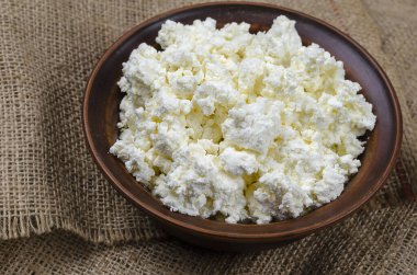 Çuval bezi üzerinde kahverengi bir kasede taze süzme peynir. Sağlıklı beslenme, mayalanmış süt ürünleri. Yakın plan. Seçici Odaklanma.