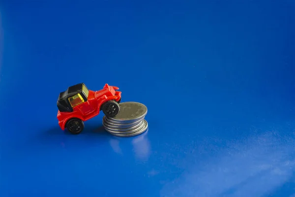 Car credit, transportation, and finance concept. Model of a toy retro car and a stack of coins on a blue background. Selective Focus.