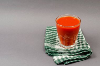 Bir bardak domates suyu ve gri arka planda yeşil kareli peçete. İçmeye hazır içecekler. Bir açıdan yan görüş. Seçici odak.