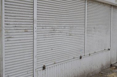 Kapalı tozlu silindirleri olan eski bir dükkan. Beyaz metalik kapalı perdeleri olan antik bir dükkan önü. Terk edilmiş bir dükkan. Seçici odaklanma. Kimse yok..